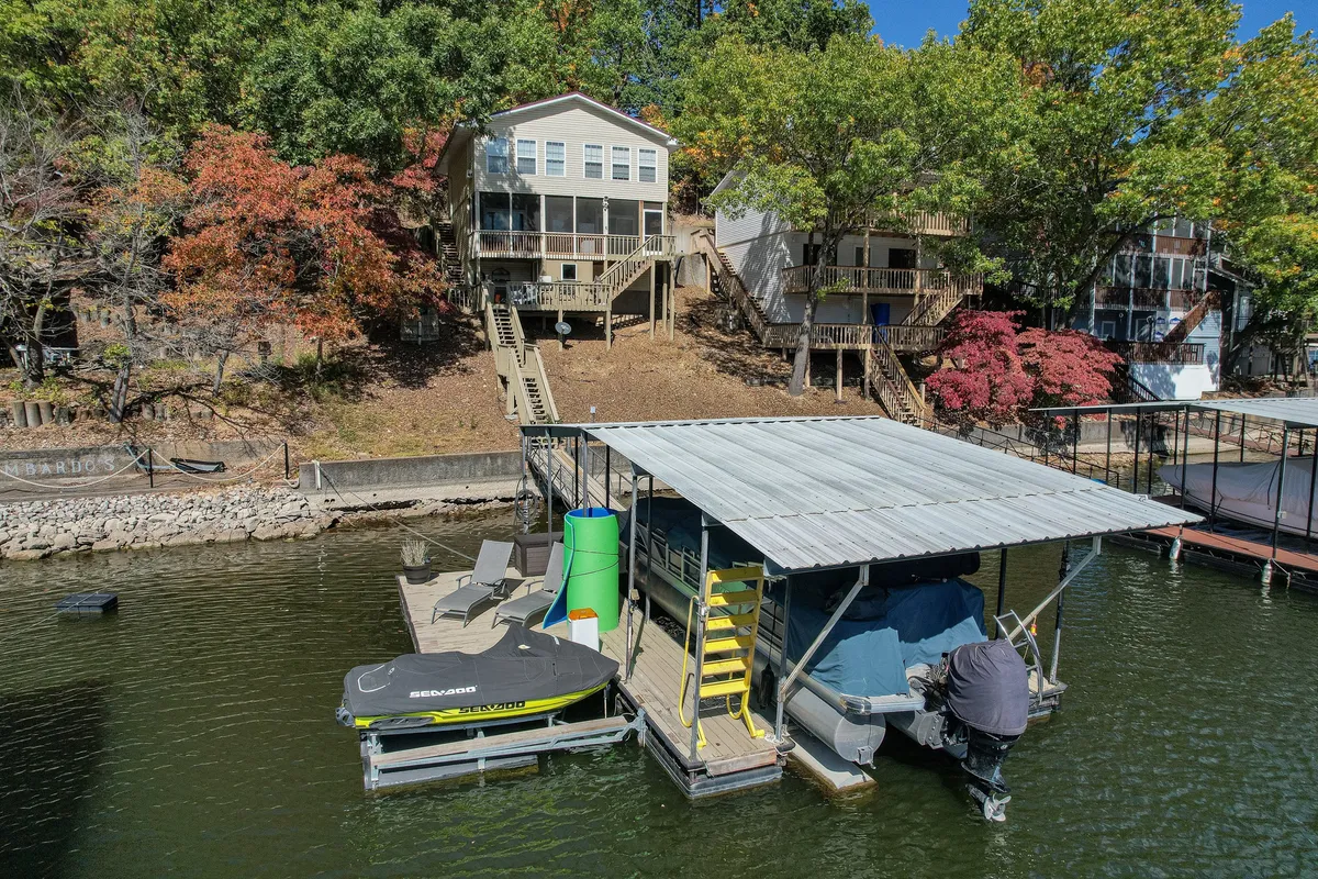 The hero image showcases a private dock with a boat lift and a colorful boat ready for adventure, set against the backdrop of tranquil lake waters, hillside homes, and vibrant autumn foliage. The scene captures the dock at sunset, inviting guests to imagine boating, fishing, sunbathing, and gathering with loved ones for cozy evenings by the fire pit.
