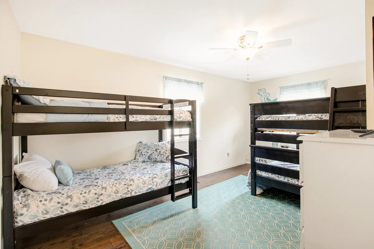 A playful, cozy bunk room featuring bunk beds, a colorful rug, and a bright window letting in natural light. The space is clearly designed with kids and teens in mind, suggesting a fun and special retreat after a day of outdoor exploration.