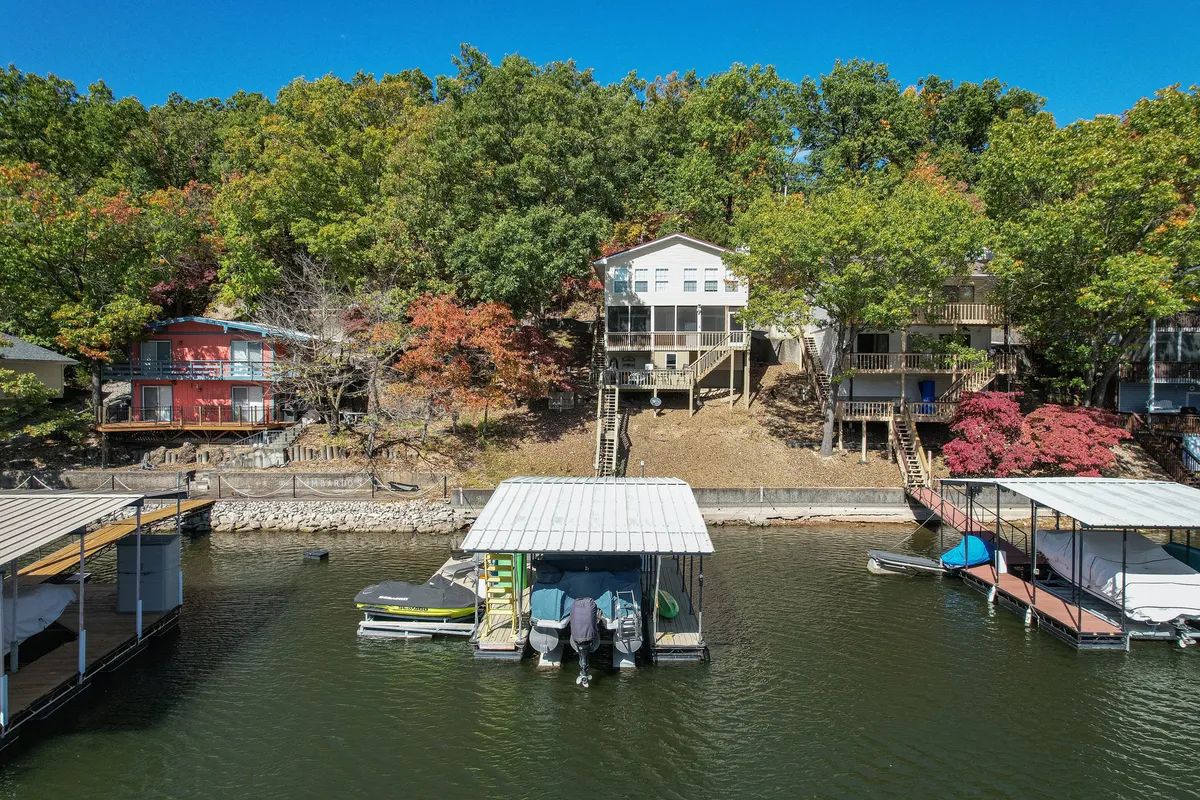 A wide exterior view of the lake framed by boathouses, with houses and trees lining the water’s edge. The scene captures a tranquil lakeside atmosphere and hints at boating, fishing, and sunset excursions.