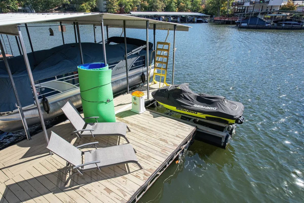 A private dock stretches out over the water, equipped with relaxation chairs, a jet ski, and a boathouse nearby. The scene showcases leisurely water activities, places to tie off a boat, and areas to bask in the sun or enjoy the peaceful view.