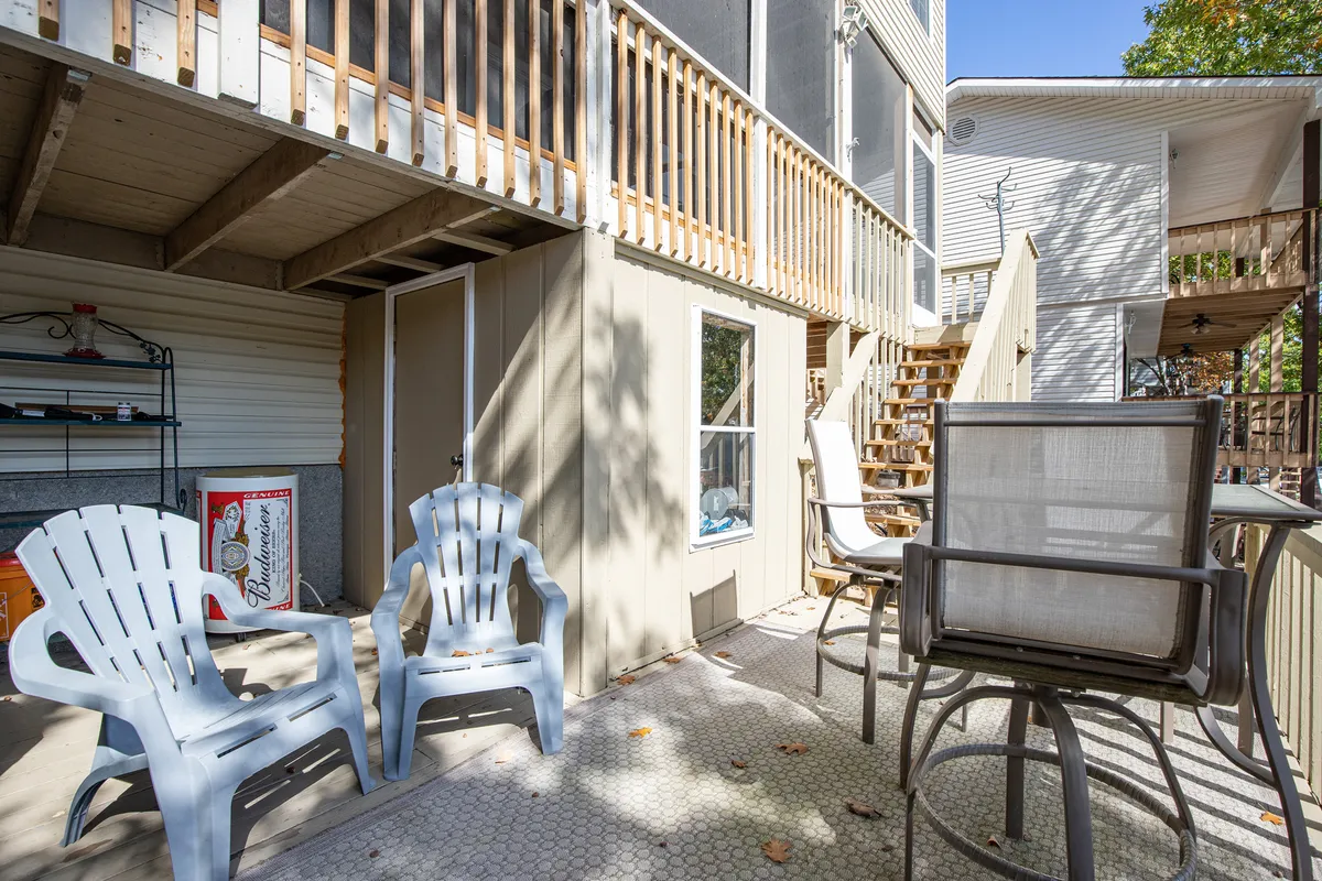 A casual outdoor space featuring Adirondack chairs, a staircase leading to an upper deck, and a storage area that hints at grilling and outdoor entertaining. The area is set for gatherings, with ample space for barbecues and shared meals while overlooking the lake.