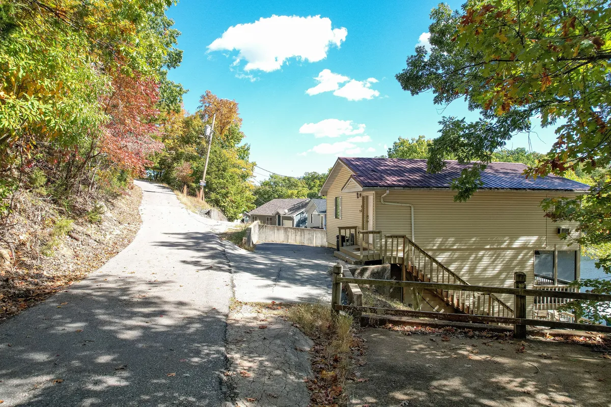 A peaceful view of the house nestled among tall trees, with a winding road leading towards it and natural surroundings abundant. The setting feels secluded yet welcoming, illustrating the blend of privacy and convenience.