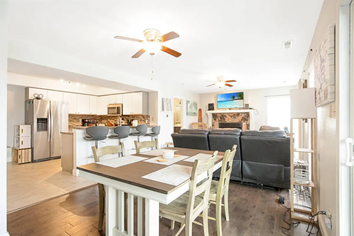 A combined living and dining space featuring a dining table, comfortable living area seating, kitchen bar stools, a fireplace, and television. The arrangement is inviting, ideal for family meals, entertaining guests, or relaxing by the fire, all within a warm and welcoming ambiance.