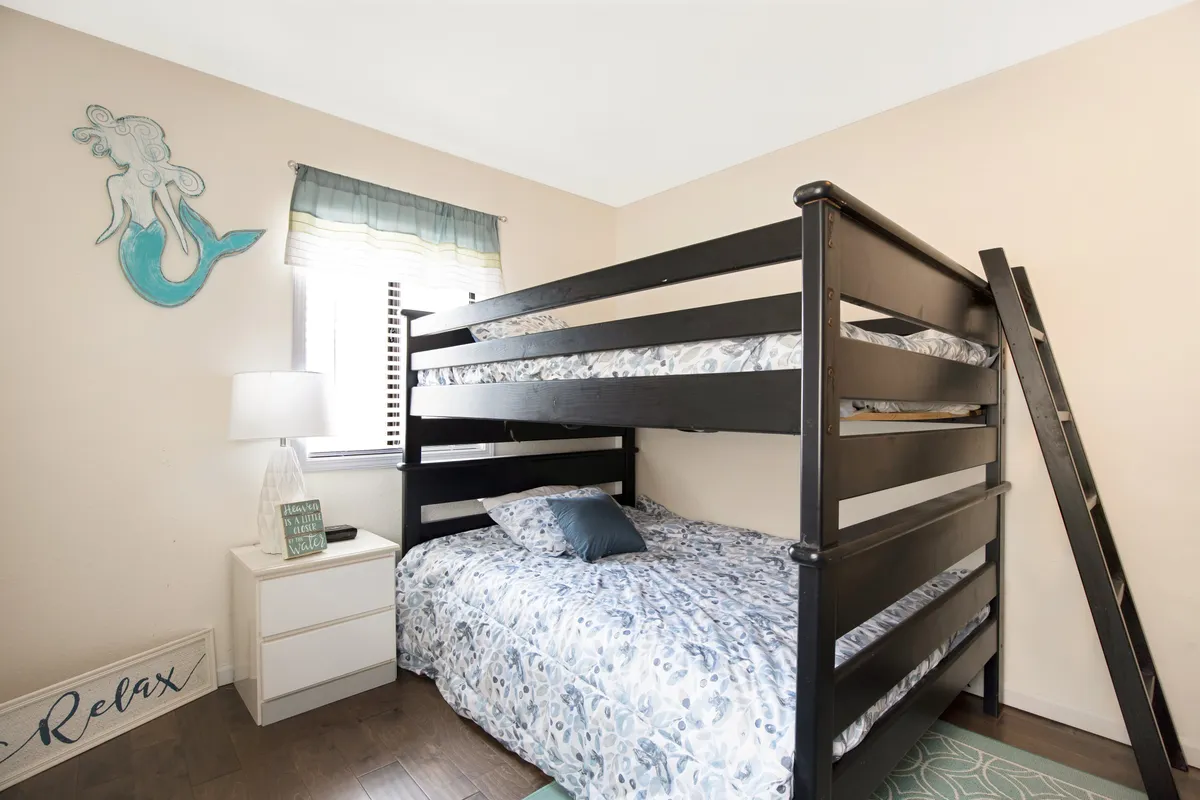 A playful, family-friendly bunk room showcasing a bunk bed, whimsical mermaid wall art, a lamp, and a nightstand. The mood is both cozy and inviting, designed for memorable sleepover stories and fun bedtime adventures.