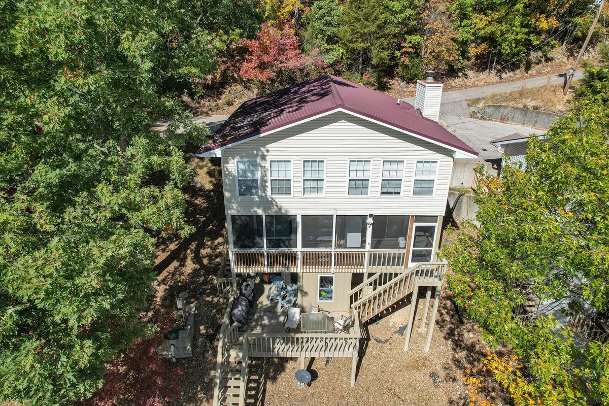 A broad view of the deck and screened porch, set amid tall trees, offering multiple outdoor living areas. The image captures both sunny and shaded spots for relaxation and socializing, underscoring the layered experience of lake life.