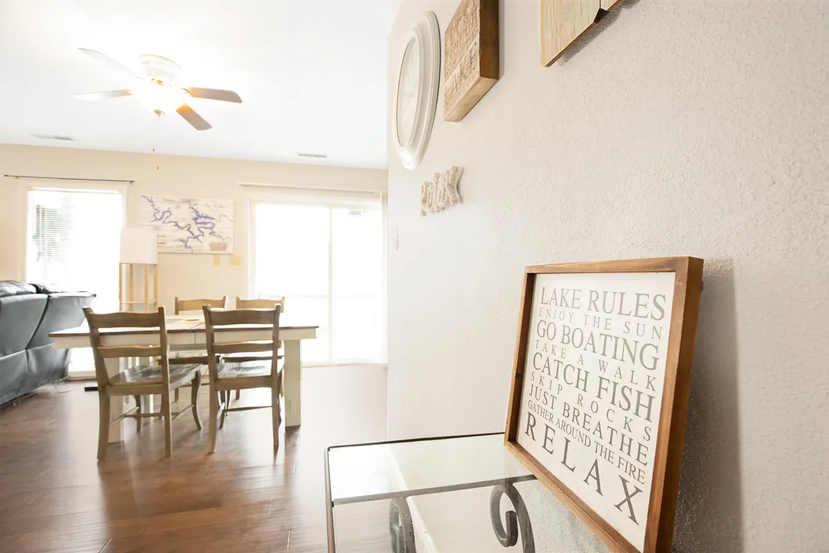 A cozy dining area with a wooden table, a 'lake rules' sign on the wall, and framed art, evoking a casual and welcoming atmosphere perfect for shared meals and group activities.